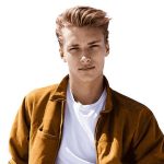 A young man with light hair styled back, wearing a white t-shirt and a brown jacket, looks confidently at the camera against a plain white background.